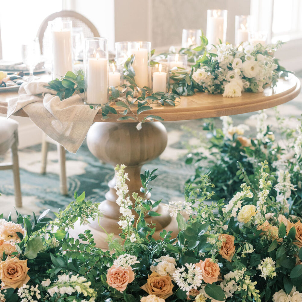 PLANNING COLLECTIONS. wedding sweetheart table covered in greenery, plus yellow, pink and white flowers - all sitting on a light wood table with pillar candles