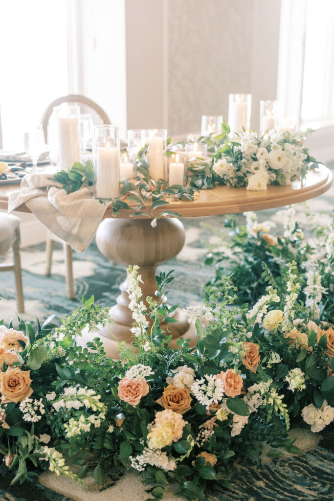 PLANNING COLLECTIONS. wedding sweetheart table covered in greenery, plus yellow, pink and white flowers - all sitting on a light wood table with pillar candles