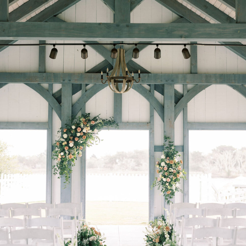 PLANNING COLLECTIONS. coastal wedding ceremony site overlooking inter-coastal waterway, with pink, yellow, and white flowers and lush greenery. White resin folding chairs.